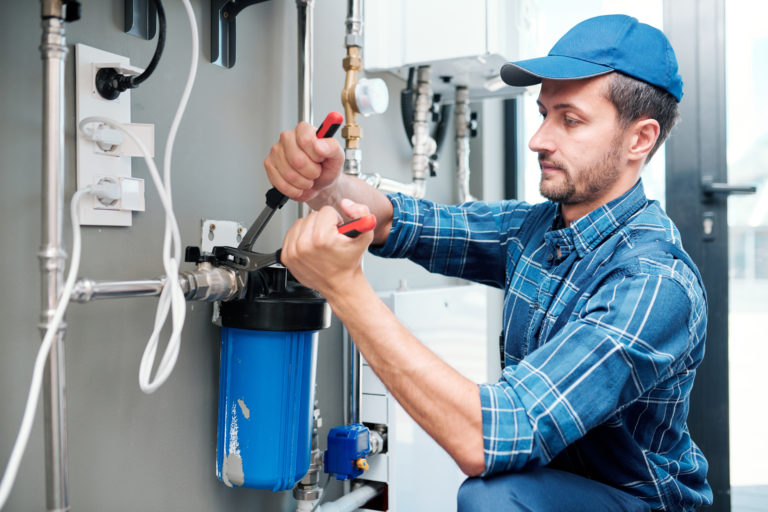 Young plumber or technician in workwear using pliers while installing or repairing system of water filtration